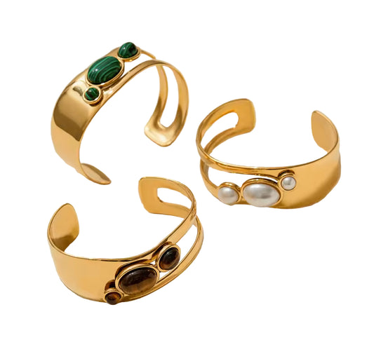 Three gold cuffs with gemstone accents on a light beige background